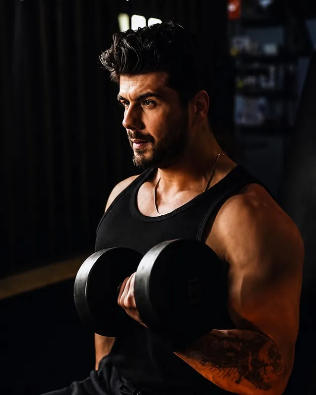 Loş ışıkta oturarak dambılla kol çalışan bir sporcu